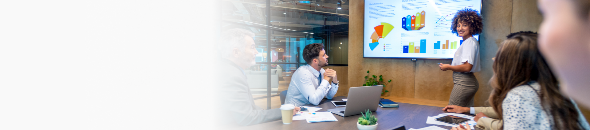 A presenter shares colorful charts and graphs on a screen during a meeting in a modern office.