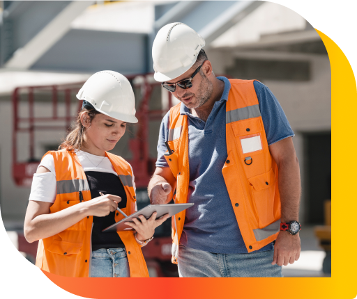 Two construction workers in orange vests and helmets with a tablet.